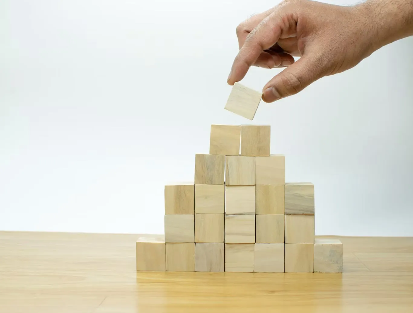 A hand adding a wooden block to a stepped arrangement of cubes.