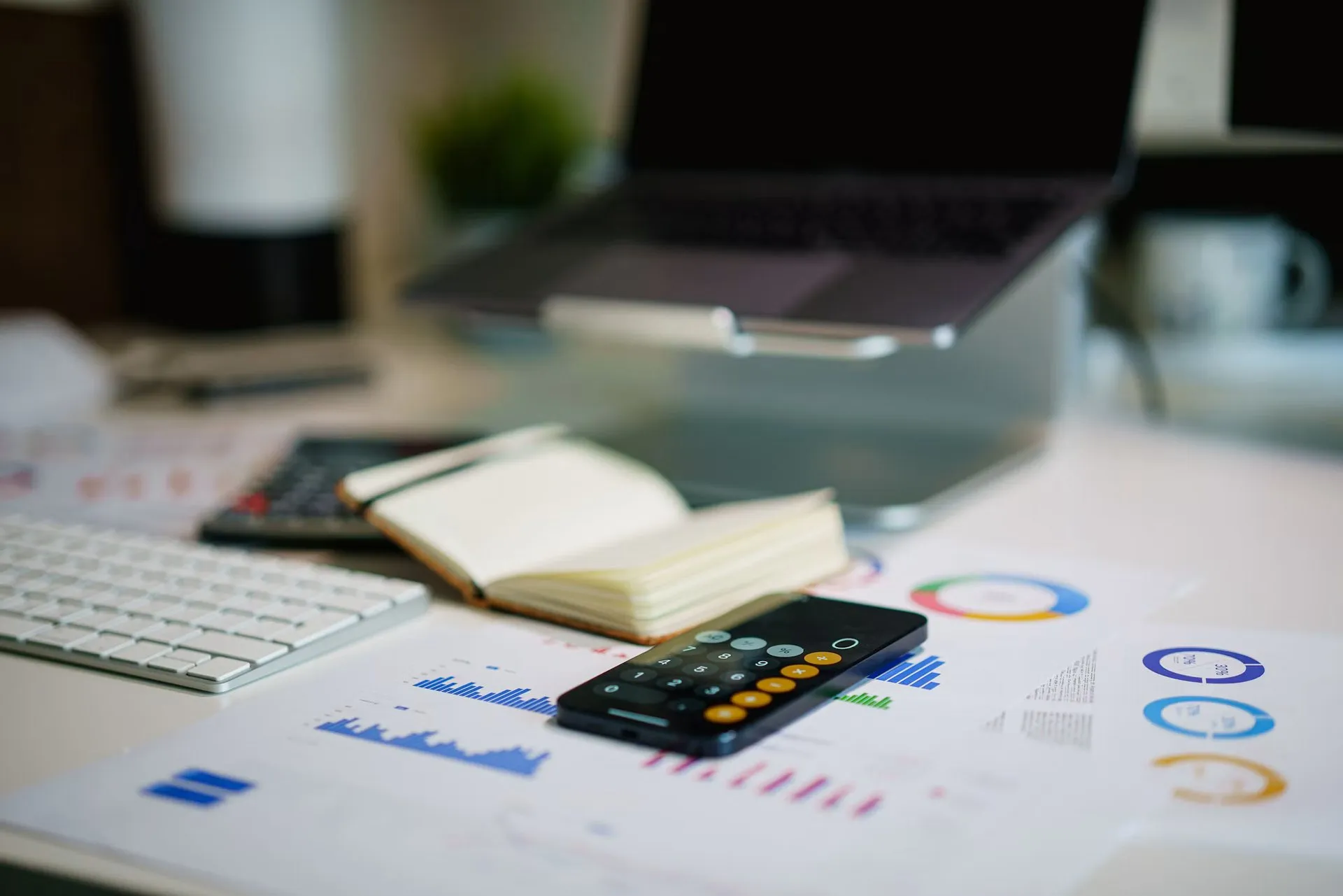 A phone calculator, notebook and printed financial charts arranged on an office desk.