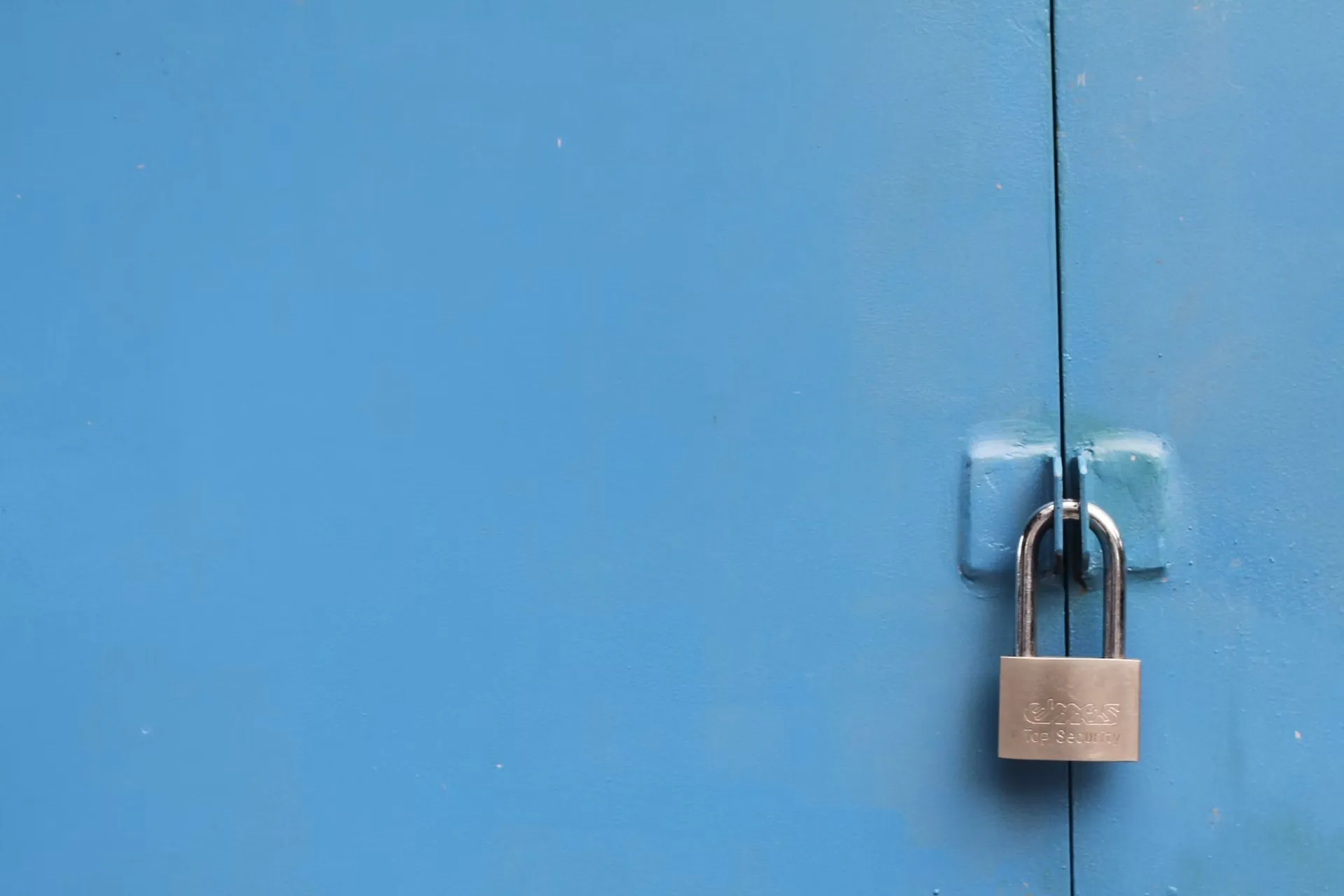 A closed metal padlock securing blue cabinet doors.