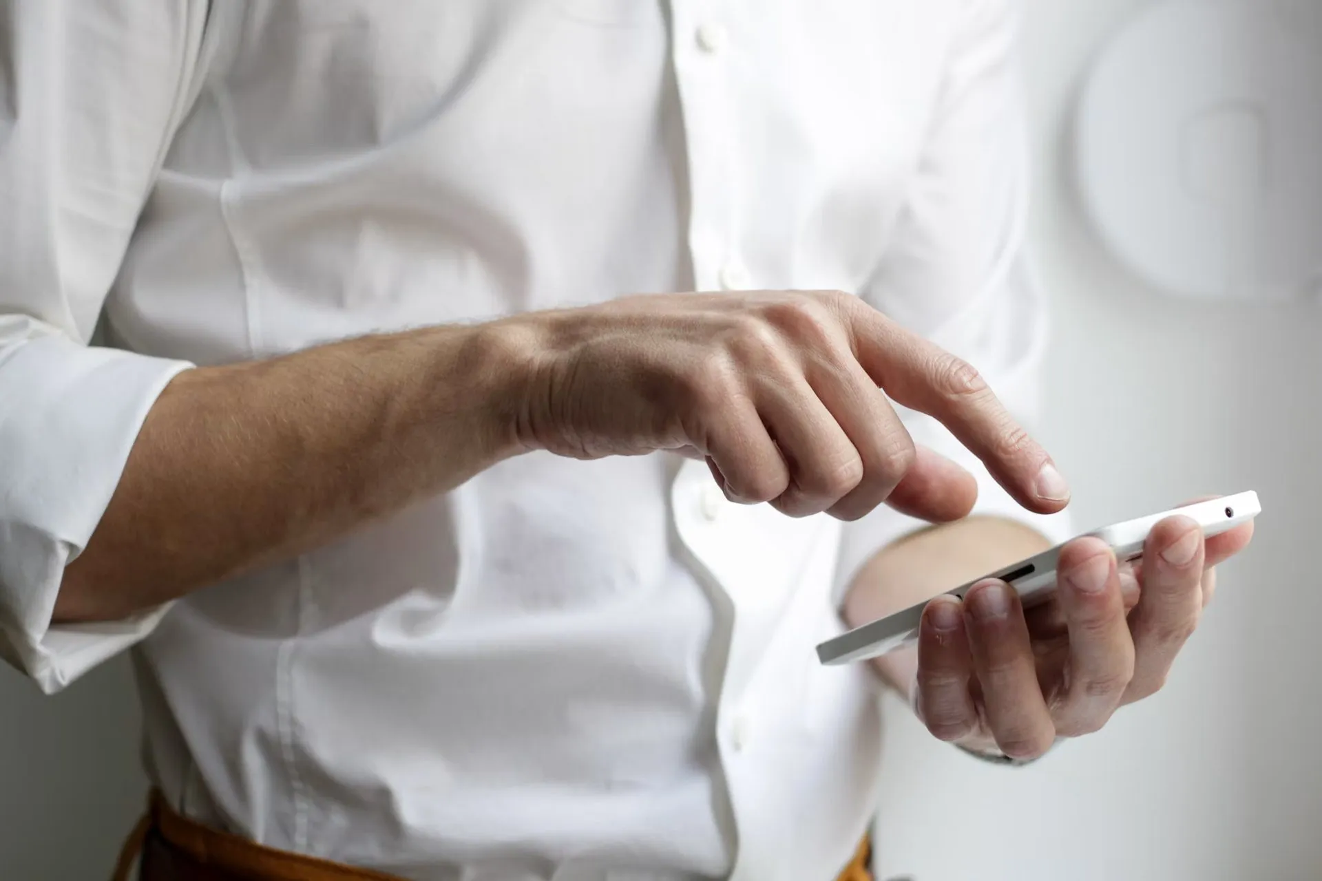 A person in a white shirt taps a smartphone held in one hand.