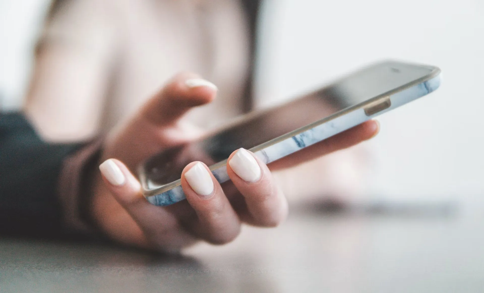 A hand holding a smartphone with a marble-patterned case in a bright room.
