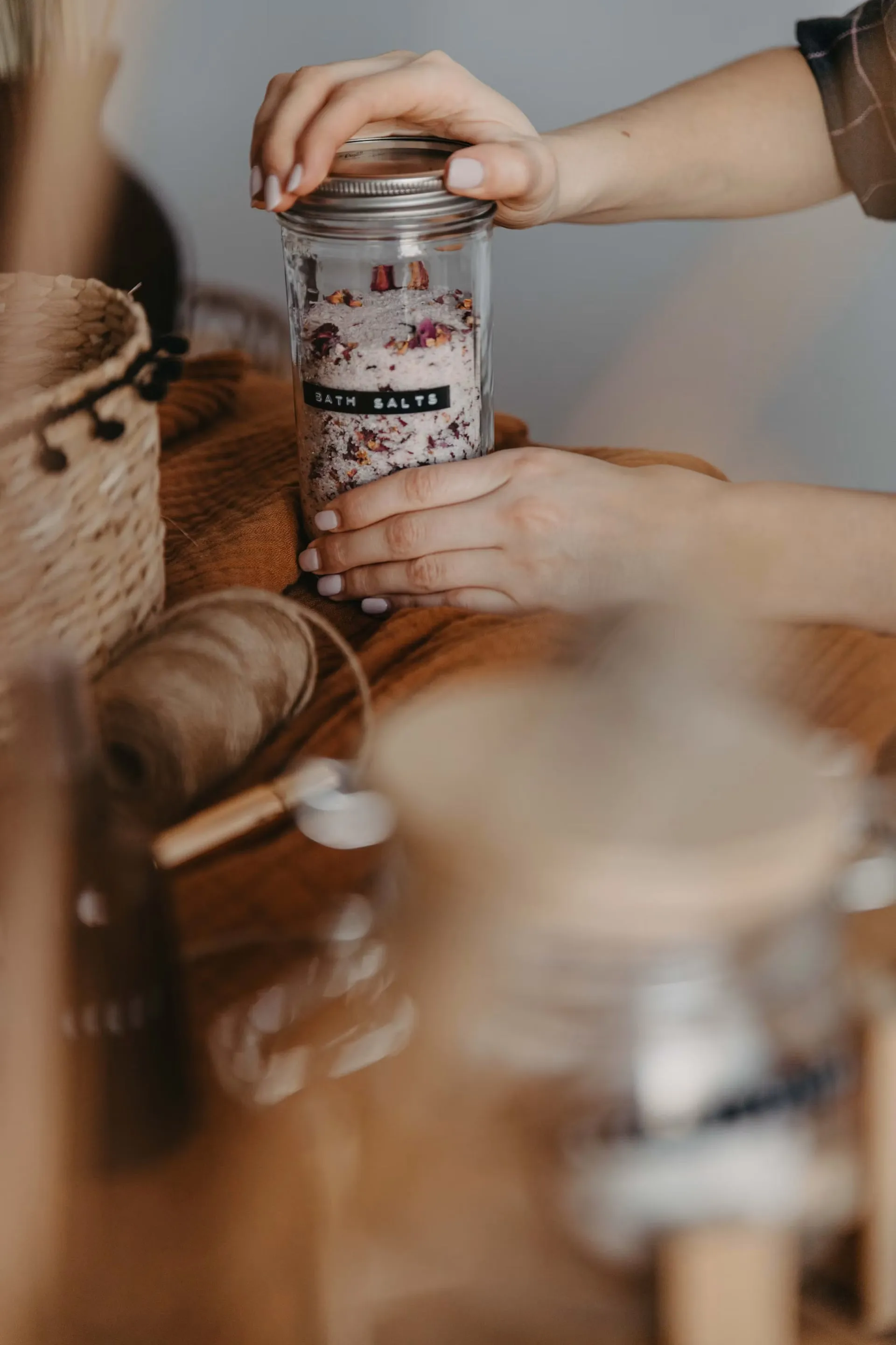Hands close a refillable jar of bath salts beside other household supplies.