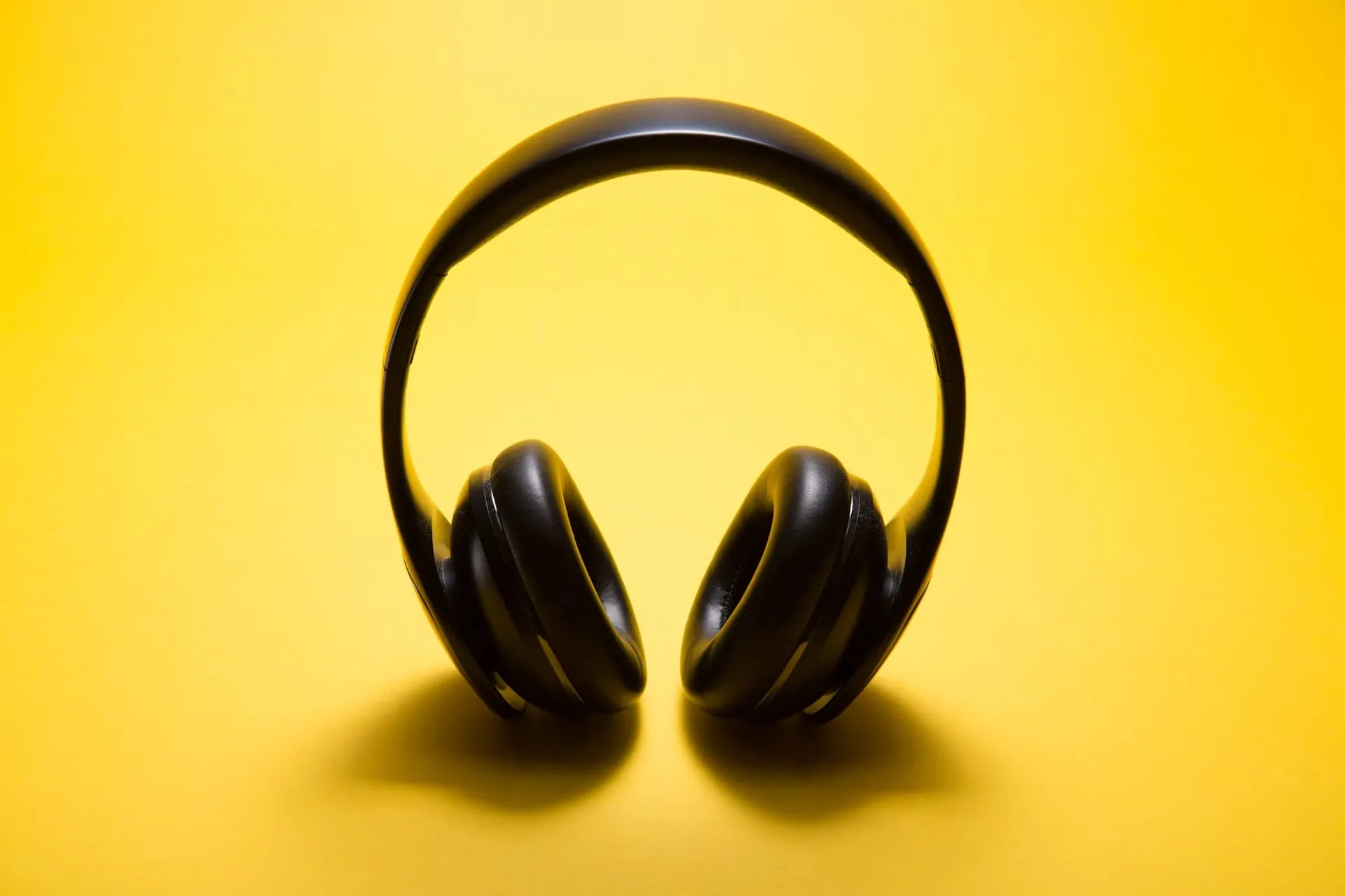 Black wireless headphones displayed on a bright yellow background.