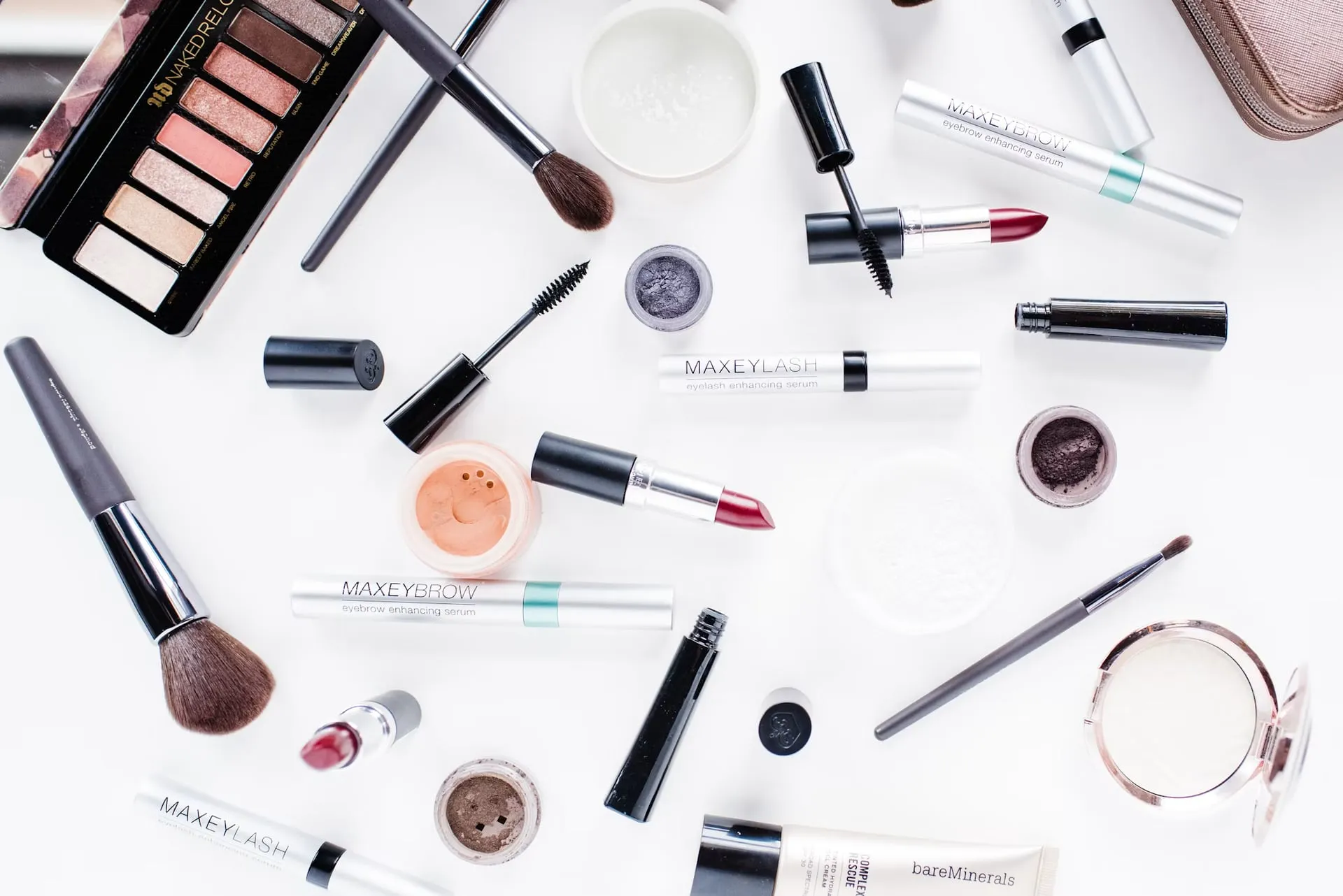 Makeup brushes, lipsticks, eyeshadow, and other beauty products arranged on a white surface.