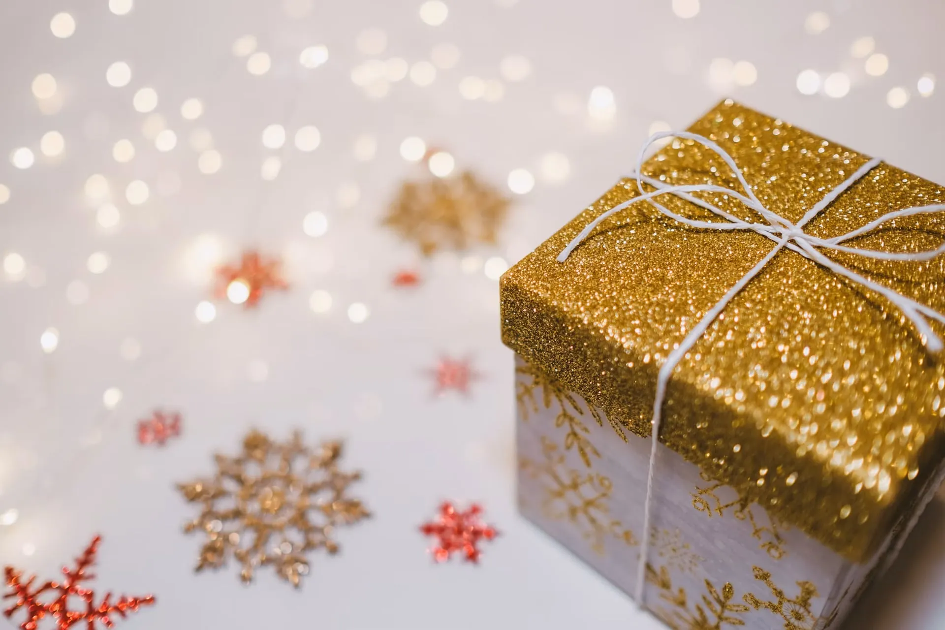 A wrapped gold holiday gift sits beside decorative snowflakes and lights.