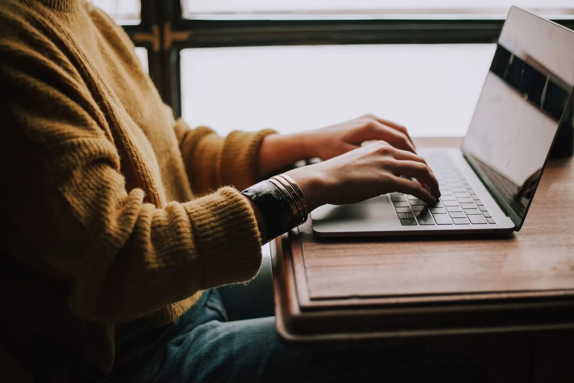 A person using a laptop beside a window.